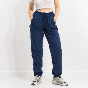 May include: Navy blue sweatpants with a drawstring waist and elastic cuffs. The sweatpants have two zippered pockets on the sides.