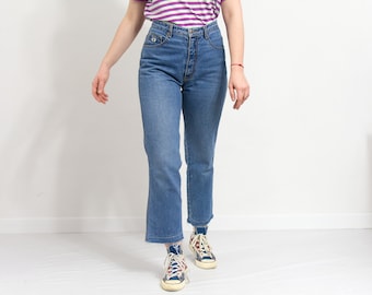 May include: A person wearing a pair of blue denim jeans with a high waist and a straight leg fit. The jeans have a frayed hem and are paired with blue and white sneakers.