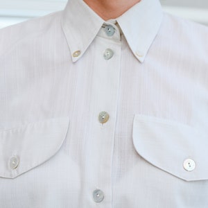 May include: A white button-down shirt with two chest pockets and pearl-like buttons.