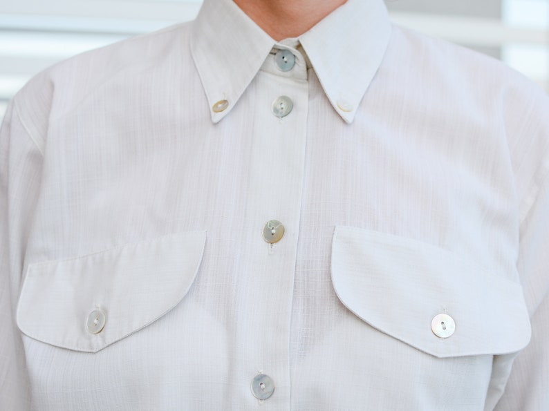 May include: A white button-down shirt with two chest pockets and pearl-like buttons.
