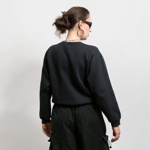 May include: A black crew neck sweatshirt with long sleeves. The sweatshirt is paired with black cargo pants. The person is wearing sunglasses and silver hoop earrings. A silver chain necklace is also visible.