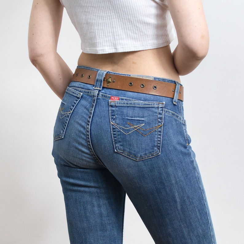 Peut inclure: Jean bleu en denim avec une ceinture en cuir marron. Le jean a une conception classique &agrave; cinq poches avec des coutures d&eacute;coratives sur les poches arri&egrave;re. La ceinture a une boucle m&eacute;tallique et plusieurs trous.