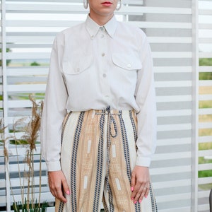 May include: A white long-sleeved button-down shirt with two chest pockets and a pair of beige and brown striped pants.