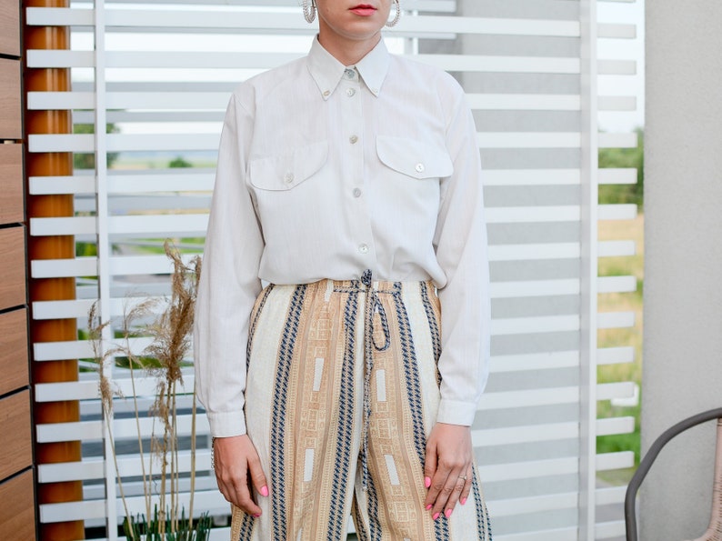 May include: A white long-sleeved button-down shirt with two chest pockets and a pair of beige and brown striped pants.