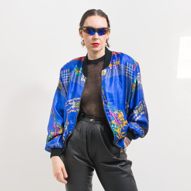 May include: A blue satin bomber jacket with a colorful, abstract print. The jacket has a zipper closure and a stand-up collar.