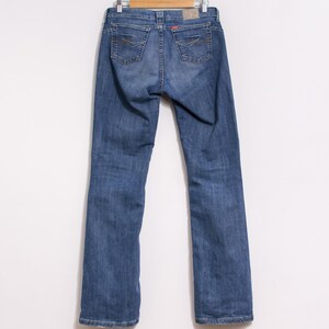 Peut inclure: Jean bleu en denim suspendu &agrave; un cintre en bois. Le jean a une conception classique &agrave; cinq poches, avec des coutures d&eacute;coratives sur les poches arri&egrave;re. Une &eacute;tiquette rouge est visible sur la ceinture arri&egrave;re. Le jean est de couleur moyenne.