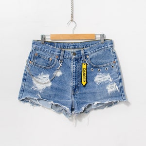 May include: Distressed denim shorts with a yellow tag that says "DANGER" hanging from the waistband. The shorts have a silver chain attached to the front pockets.