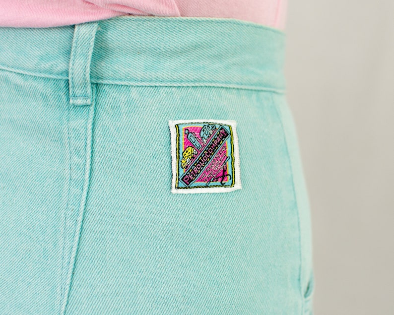 Puede incluir: Un par de pantalones vaqueros de color azul claro con un peque&ntilde;o parche rectangular en el bolsillo trasero derecho. El parche es blanco con detalles en rosa, amarillo y azul y dice "Petrolicious" en rosa.