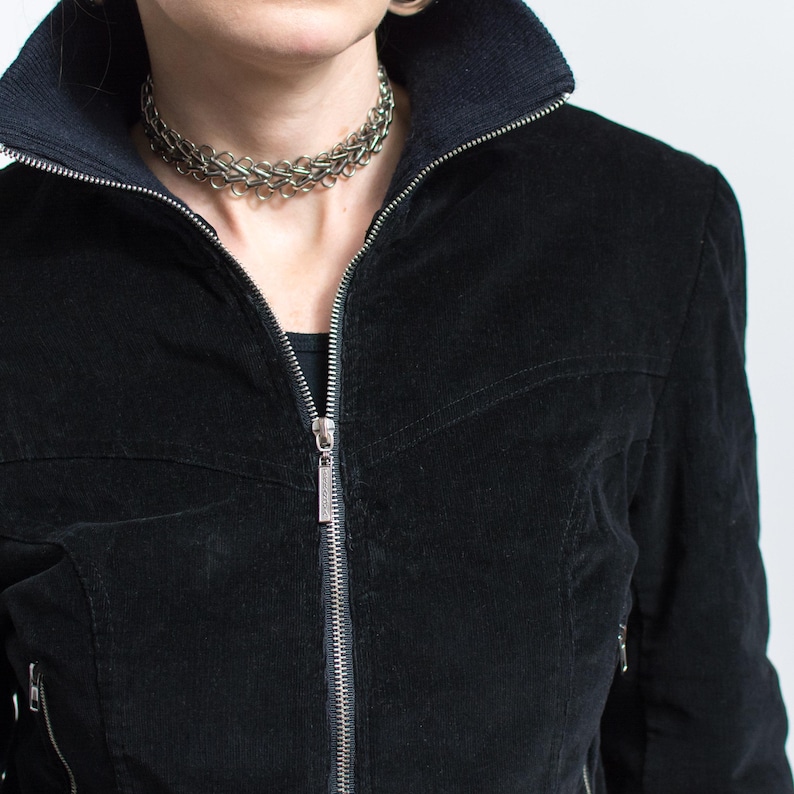 Puede incluir: Chaqueta de pana negra con cremallera plateada y cuello acanalado. La chaqueta tiene una silueta entallada y un collar de cadena plateada. Un estilo cl&aacute;sico, adecuado para diversas ocasiones.