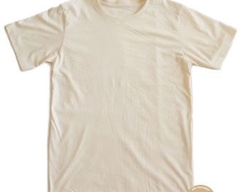 Könnte beinhalten: Cremefarbenes T-Shirt mit kurzen Ärmeln und Rundhalsausschnitt. Das T-Shirt hat ein schlichtes, klassisches Design. Ein kleines, rundes Logo mit Text ist in der unteren rechten Ecke sichtbar. Das Shirt scheint aus einem weichen, natürlichen Stoff zu sein.