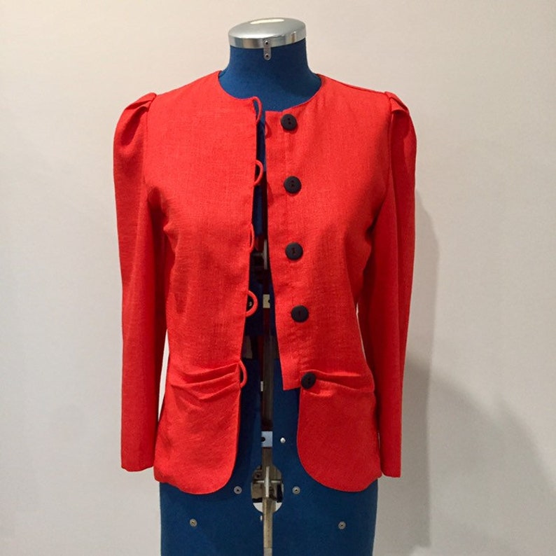 May include: A red blazer with long sleeves and a button-up front. The blazer has a round neckline and black buttons.