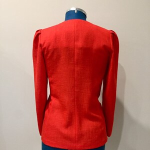 May include: A red blazer with long sleeves and a slightly puffed shoulder detail. The blazer is on a mannequin.