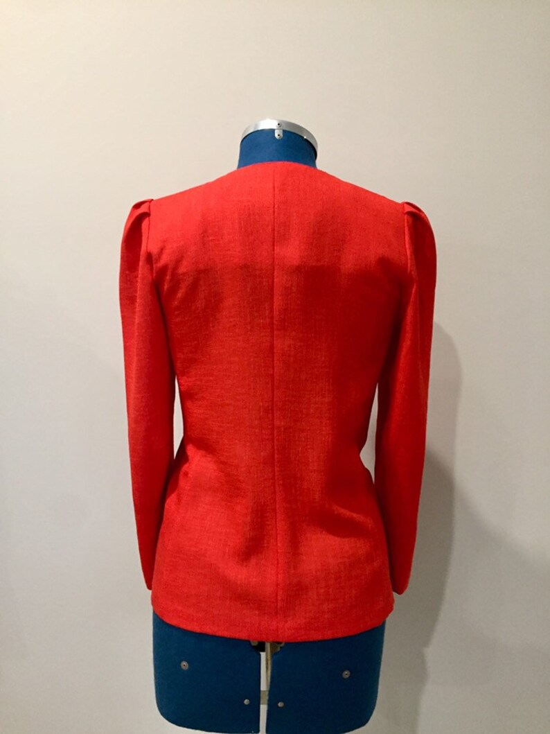 May include: A red blazer with long sleeves and a slightly puffed shoulder detail. The blazer is on a mannequin.
