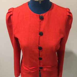 May include: A red linen blazer with a round neckline and five black buttons. The blazer has puffed sleeves and a fitted waist.