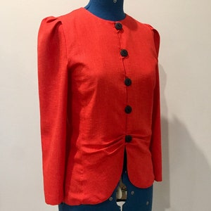 May include: A red linen blazer with a button-up front and long sleeves. The blazer has a slightly puffed shoulder and a fitted waist.