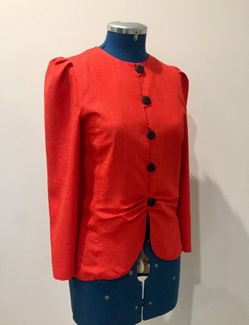 May include: A red linen blazer with a button-up front and long sleeves. The blazer has a slightly puffed shoulder and a fitted waist.
