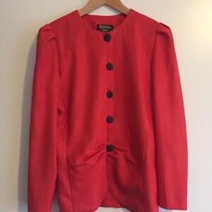 May include: A red blazer with a round neckline and five black buttons. The blazer has a gathered detail at the waist.