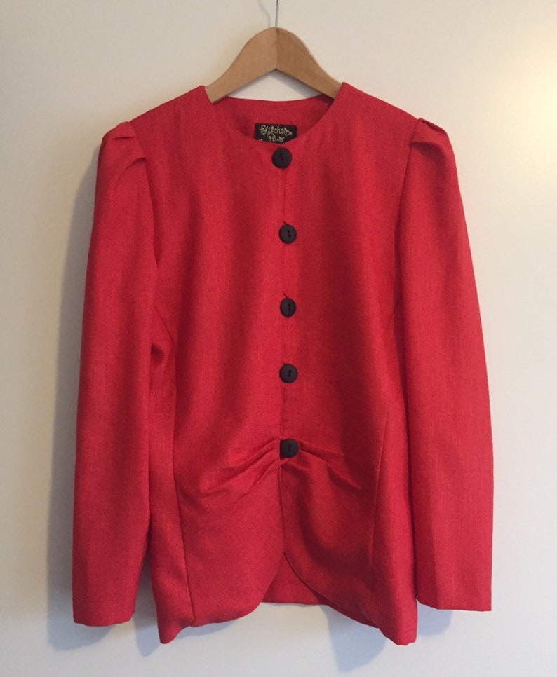 May include: A red blazer with a round neckline and five black buttons. The blazer has a gathered detail at the waist.
