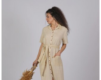 May include: A beige linen dress with a button-down front, short sleeves, and a belt. The dress has a slit up the front and pockets on the sides.