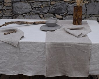 May include: A white linen tablecloth with a beige linen table runner. A small grey bowl and a plate are on the table. A wooden branch and a small piece of wood are also on the table.