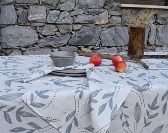 May include: A white tablecloth with a gray leaf pattern and orange and green dots. The tablecloth is laid out on a table with gray ceramic bowls and red apples.