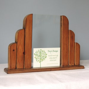May include: A wooden picture frame with a unique, art deco design. The frame is made of multiple pieces of wood, creating a layered effect. The frame is standing on a white surface.
