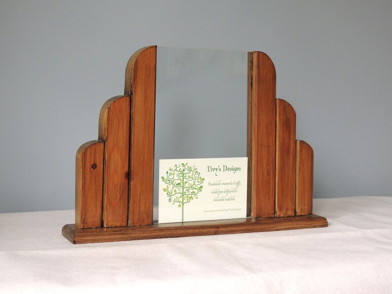 May include: A wooden picture frame with a unique, art deco design. The frame is made of multiple pieces of wood, creating a layered effect. The frame is standing on a white surface.