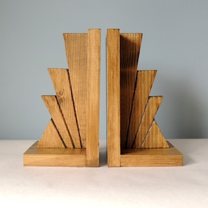 May include: A pair of wooden bookends with a sunburst design. The bookends are made of natural wood and have a light brown finish.