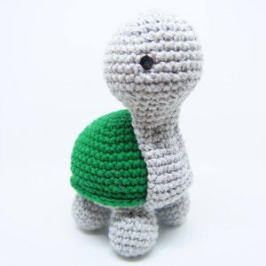 May include: A crocheted turtle toy with a gray body and green shell. The turtle has a single black eye.