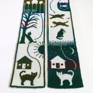 May include: A white knit scarf with a green and blue ombre design. The scarf features a repeating pattern of cats, houses, and a sun and moon. The text "Nifty Knitter Designs" is printed on the scarf.