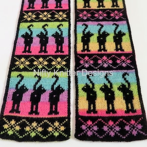 Op de afbeelding: Een zwarte en regenboogkleurige gebreide sjaal met een herhalend patroon van zwarte katten. De sjaal is gemaakt van zacht, pluche garen en heeft franjes aan de uiteinden.