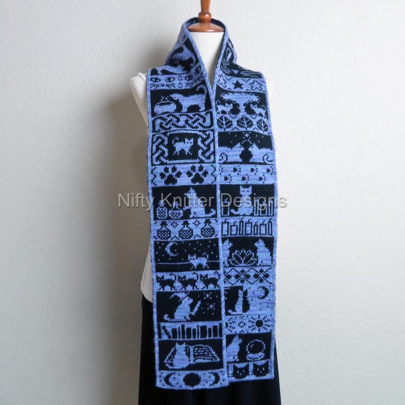 May include: A blue and black knitted scarf with a repeating pattern of cat-themed designs. The scarf is displayed on a mannequin and features various cat silhouettes, paw prints, and other related motifs. The text "Nifty Knitter Designs" is visible.