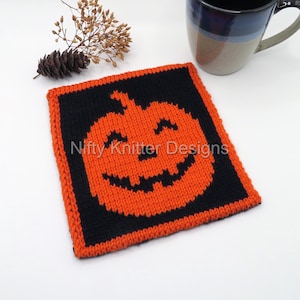 May include: A square, knitted Halloween coaster featuring an orange jack-o'-lantern design on a black background. The coaster has an orange border and the text "Nifty Knitter Designs". A mug is in the background.