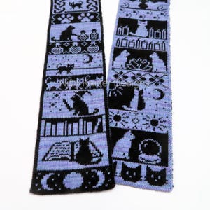 May include: A knitted scarf with a repeating pattern of black cats, moons, stars, and other whimsical designs on a light purple background. The scarf is made of soft yarn and is perfect for cat lovers.