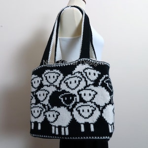 May include: A black and white knitted tote bag with a pattern of sheep faces. The bag has two black straps.