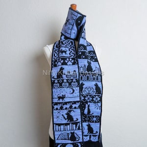 May include: A blue and black knitted scarf with a hood, featuring a repeating pattern of cat silhouettes, candles, and books. The scarf is displayed on a mannequin. The design includes Celtic knots and paw prints. The scarf is approximately 72 inches long.