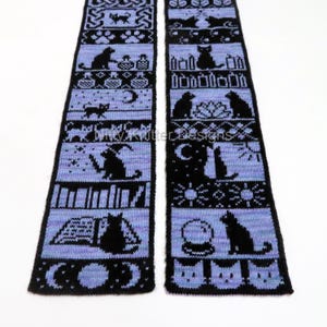May include: A black and periwinkle knitted scarf featuring repeating patterns of cats, moons, books, and other witchy symbols. The text "Kitty Knitter Designs" is visible on the scarf. The scarf is displayed on a white background.