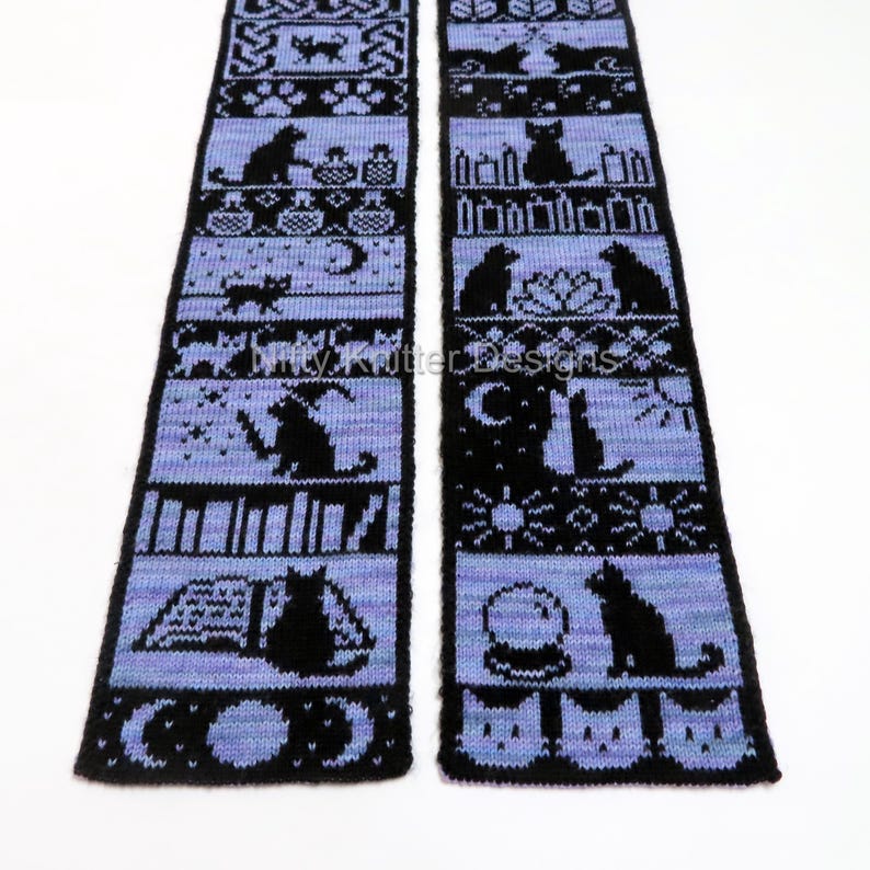 May include: A black and periwinkle knitted scarf featuring repeating patterns of cats, moons, books, and other witchy symbols. The text "Kitty Knitter Designs" is visible on the scarf. The scarf is displayed on a white background.