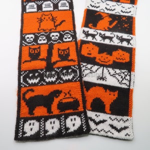 May include: A pair of orange, black, and white knitted scarves with a Halloween theme. The scarves feature various Halloween motifs, including cats, pumpkins, ghosts, and skulls.