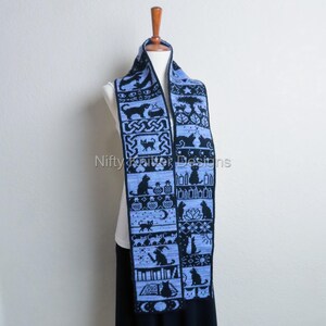 May include: A light blue and black knitted scarf featuring a repeating pattern of black cat silhouettes, moons, and other whimsical designs. The scarf is displayed on a mannequin and has the text "Nifty Knitter Designs".