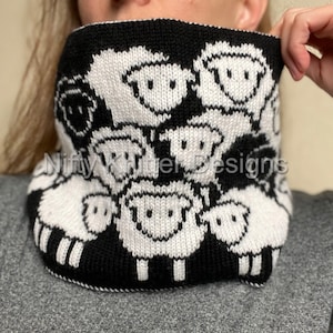 May include: Black and white knitted cowl featuring a pattern of sheep faces. The cowl is made from a soft, warm yarn and is ideal for keeping warm during the winter months.
