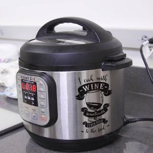 May include: A stainless steel Instant Pot electric pressure cooker with a black lid and a black and white vinyl sticker that reads "I cook with wine sometimes I even add it to the food".