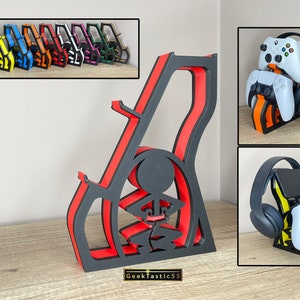 May include: A black and red 3D printed stand with a stick figure holding a controller. The stand is designed to hold a headset, two controllers, and a phone. The stand is labelled "GeekTastic55".
