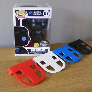 May include: A black and blue Superman Pop! Vinyl figure in a box with a glow in the dark feature. The figure is displayed with four different colored plastic stands, red, white, blue, and black.