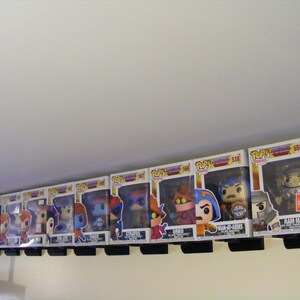 May include: A collection of 11 Masters of the Universe Pop! figures displayed on a shelf. The figures include He-Man, Battle Cat, Man-At-Arms, Ram Man, Orko, Skeletor, Beast Man, Trap Jaw, Stratos, Faker, and Evil-Lyn. The figures are all in their original packaging.