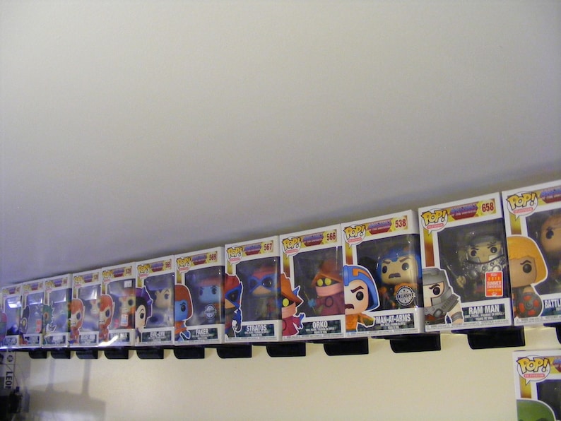 May include: A collection of 11 Masters of the Universe Pop! figures displayed on a shelf. The figures include He-Man, Battle Cat, Man-At-Arms, Ram Man, Orko, Skeletor, Beast Man, Trap Jaw, Stratos, Faker, and Evil-Lyn. The figures are all in their original packaging.