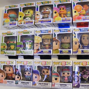 May include: A collection of Funko Pop! vinyl figures displayed on a shelf. The figures include characters from The Muppets, Teenage Mutant Ninja Turtles, The Emperor's New Groove, Wreck-It Ralph, and more.