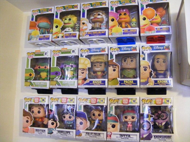 May include: A collection of Funko Pop! vinyl figures displayed on a shelf. The figures include characters from The Muppets, Teenage Mutant Ninja Turtles, The Emperor's New Groove, Wreck-It Ralph, and more.