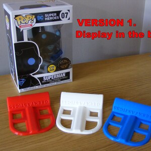 May include: Three 3D printed plastic display stands in red, white, and blue. The stands are designed to hold a Funko Pop figure in a box. The text "GEEKTASTIC55" is printed on each stand.