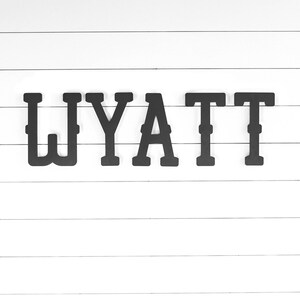 May include: Black wooden letters spelling out the name "WYATT" on a white wood background.